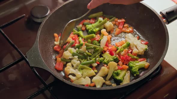 Caucasian Hand Stirring Vegetables in a Frying Pan with Stainless Steel Spoon While Frying Closeup