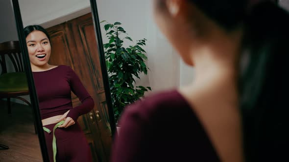 Over Shoulder Portrait of Excited Asian Woman Checking Weight Loss with Measuring Tape and Enjoying alt