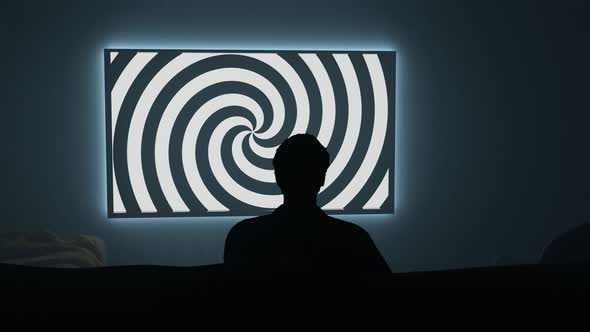 Darkroom with person watching TV with a hypnotic spiral on the screen. 4K render alt