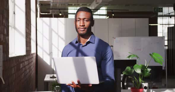 African american businessman holding laptop looking ahead shifting gaze to camera and smiling alt