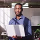 African american businessman holding laptop looking ahead shifting gaze to camera and smiling