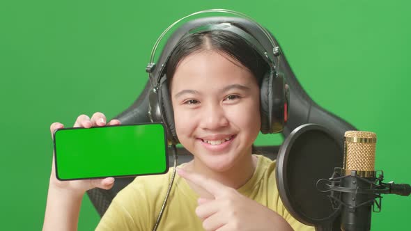 Kid Girl Holding Mobile Phone With Mock Up Green Screen While Live Stream In Green Screen Studio alt