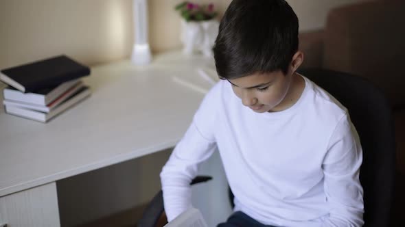 Young Boy Sitting By the Desk and Read the Book. Study at Home During Quarantine. Distance Learning