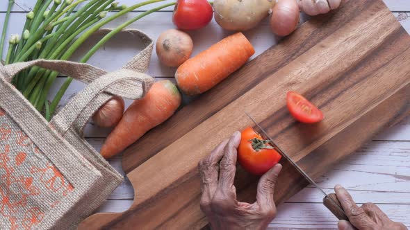 Top View of Senior Women Cutting Tomato on Chopping Board. alt