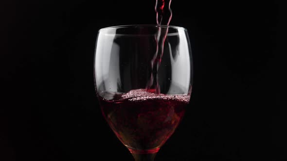 Wine. Red wine pouring in wine glass over dark background. Rose wine pouring from the bottle. Slow m