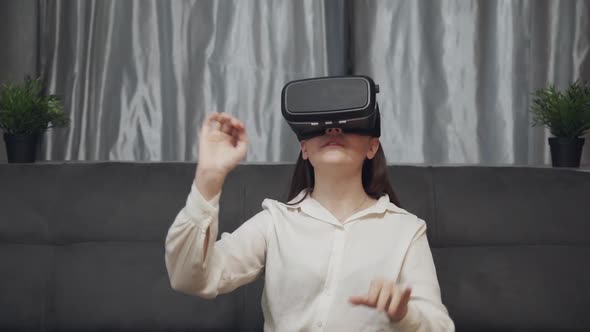Young Woman Testing Virtual Reality Glasses While Sitting on Sofa in Home Interior.