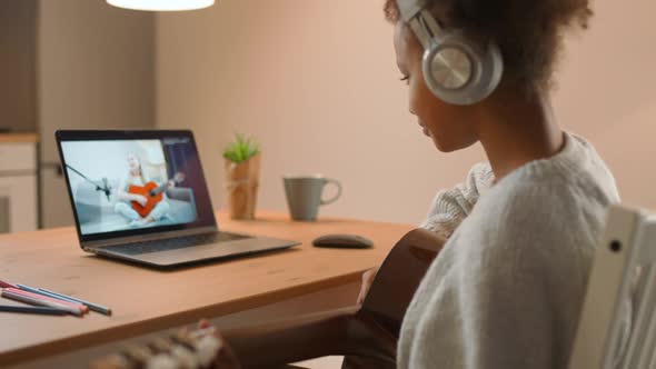 Young African Girl is Engaged in Playing the Guitar with a Teacher Using a Video Call Distance alt