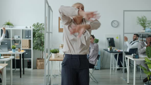 Excited Young Businesswoman Moving to Music in Office While People in Background Applauding alt