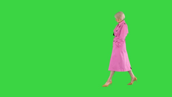 Trendy Beautiful Senior Woman in a Pink Coat Walks in and Showing Her Outfit To Camera on a Green alt
