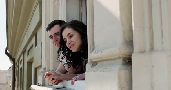 Young Couple Man and Woman Sitting on Window Sill and Enjoying Old Town View alt