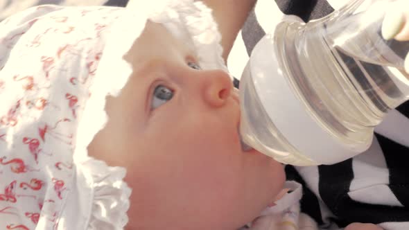 Mother giving baby girl to drink from the bottle alt