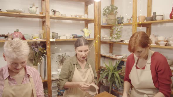 Two Senior Ladies Making Clay Bowls in Studio with Young Teacher alt