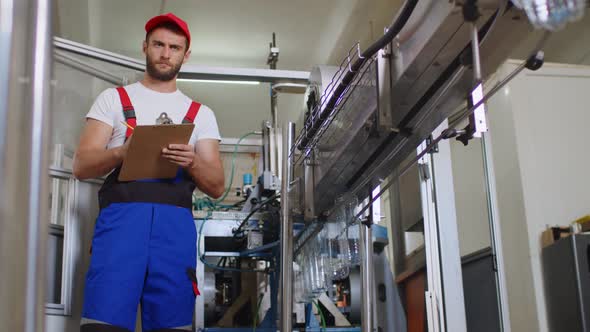 Young Factory Man in Uniform Making Notes on Clipboard at Water Production Factory