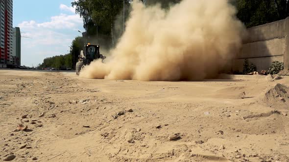 Excavator rides in slow motion. Clouds of dust. Cleaning dust from the road in the city.