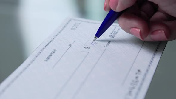 business woman hand signs and filling bank check for one thousand 1000 dollars alt