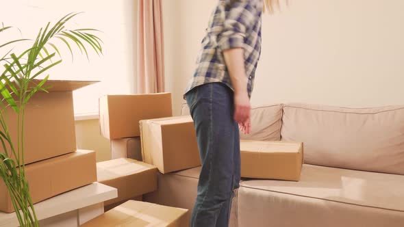 A Woman in a Plaid Shirt Puts Cardboard Boxes on the Sofa