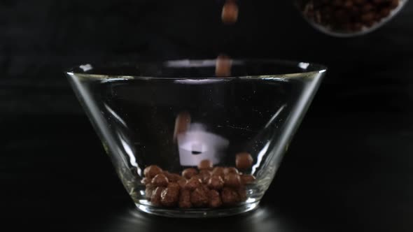 Chocolate Cereal Balls Fall in a Transparent Square Bowl on a Black Background. Close Up.