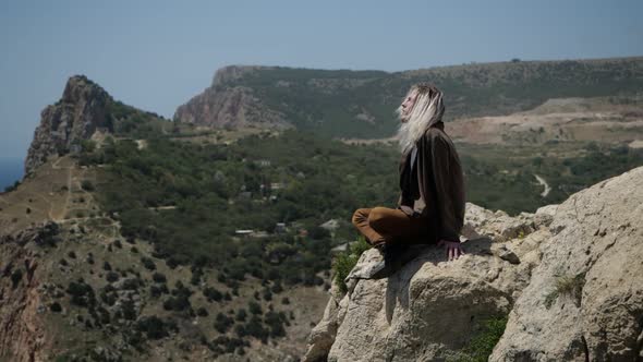 A Young Guy Sits on a Mountainside Against a Panorama of Mountains