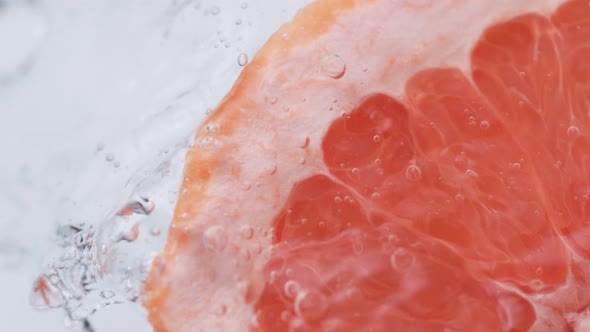 Halved pink grapefruit falling in water. Slow Motion. alt