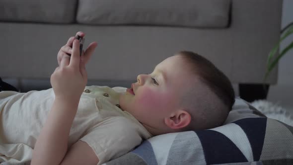 A boy lying on a bed at home, relaxing, smiling and watching video on smartphone