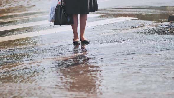 A Woman Stands on the Road and Tries to Cross the Road and Step Over Puddles After a Heavy Rain alt