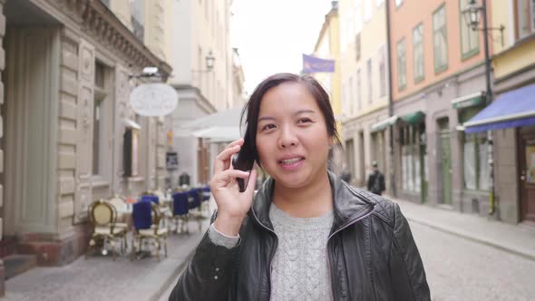 Front view of happy Asian woman walking and having a call on street in Sweden