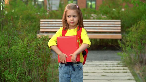Girl Holds Book in Schoolyard Smiles and Laughs