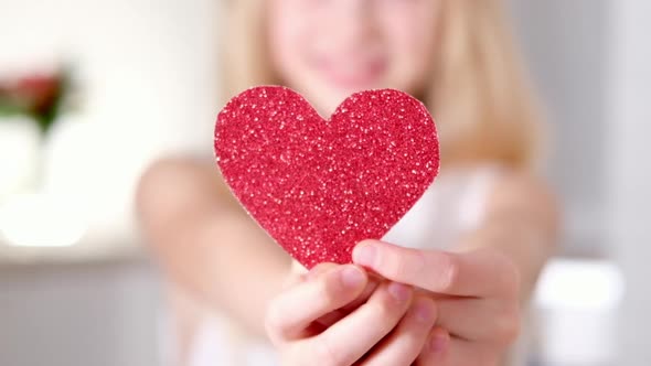 Red Heart Close Up in Hands of Little Blonde Smiling Girl on Valentines Day alt