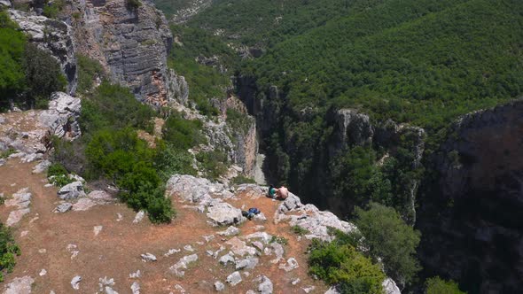 Aerial view of couple sitting on cliff top beside deep valley and enjoying the sight of Benje Canyon alt
