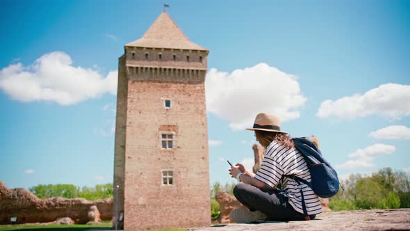 A Young Woman Using Her Smartphone While Sitting at the Historical Fortress alt
