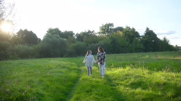 Happy young mum and daughter walking together outdoor enjoy beautiful field