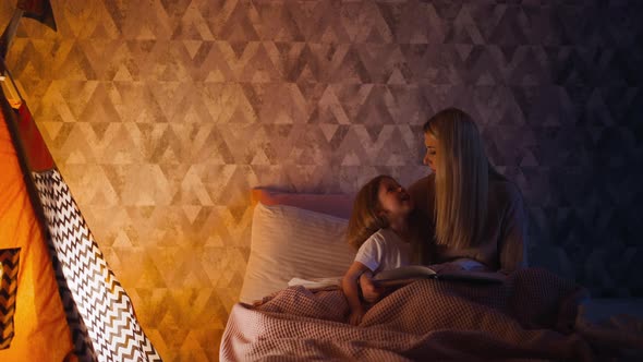 Little Girl and Mum with Book on Bed at Illuminated Wigwam alt