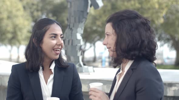 Brunette Businesswomen Drinking Coffee Outdoors and Talking alt