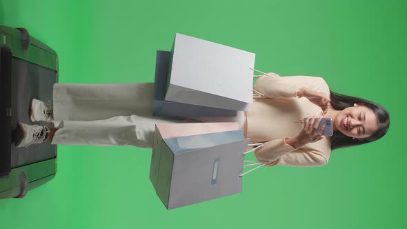 Asian Woman With Shopping Bags Use Mobile Phone While Walking On Jogging Machine On Green Screen alt