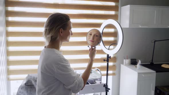 Pretty Woman Looks in Round Mirror Sitting on Couch in Room