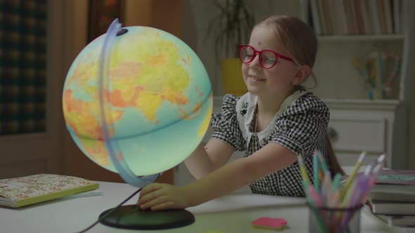 Schoolgirl Studying Geography at Home Using Earth Globe on the Table alt