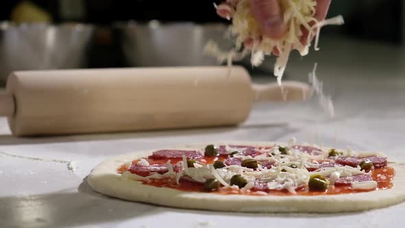 Cooking pizza in restaurant in kitchen. cook pours grated cheese on raw dough