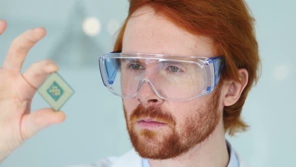 Scientist in Protective Glasses Looking at Computer Chip alt