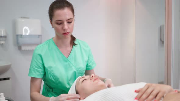 Girl Beautician Makes Facial Cleansing Procedure for Young Woman in Beauty Salon alt