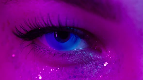 Closeup of Young Woman Eye Wearing Decorative Lenses in Ultraviolet Light Makeup with Glitter and alt