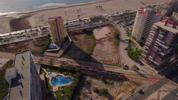 Tram light rail crossing the tracks at the coast of San Juan de Alicante at dawn. Arenal drone view alt