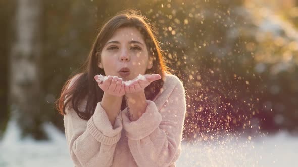 Brunette young woman blowing snow in snowy sunny evening day