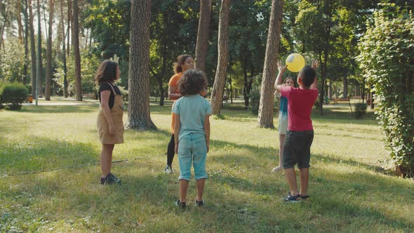 School Kids Playing Ball with Young Female Teacher in Public Park alt