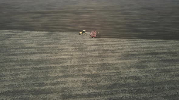 Aerial view of a modern yellow tractor plowing dry agricultural field , preparing land for sowing alt