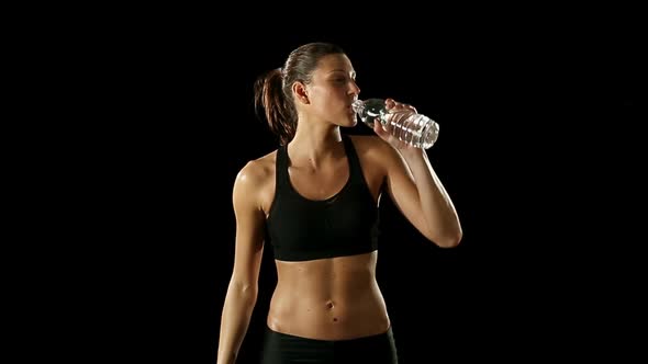 Young Athletic Woman Wearing Sporstwear is Drinking Water From Plastic Bottle Isolated on Black
