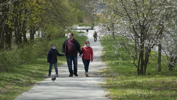 A Father and Two Daughters in Medical Masks Walk Near the Park. The Concept of Protection FROM Covid