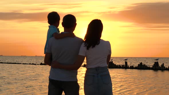 Happy Family: Father, Mother and Child Enjoy a Beautiful Sea Sunset. The Woman Hugs the Man and Puts