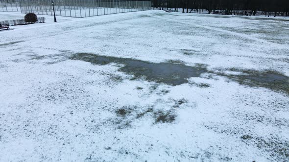 Flying over a sports field in a snow-covered city park. Aerial photography alt