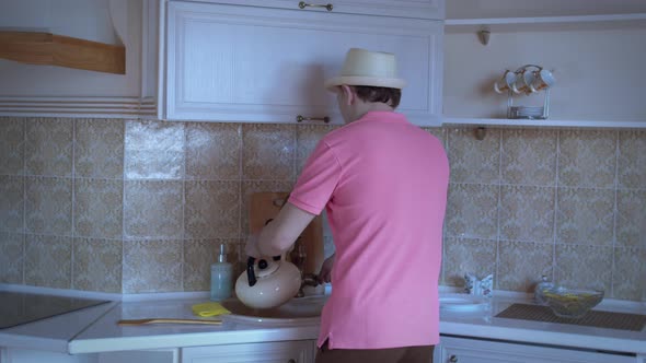 Man in a Hat is Dancing in the Kitchen Pouring Water Into a Kettle Good Mood alt