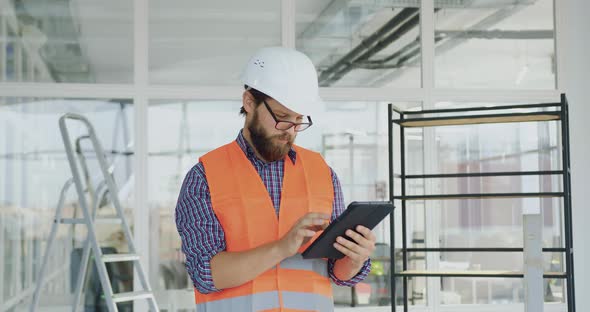 Builder in Hardhat, Gogglesand Vest Using Tablet PC in New Built Office  alt